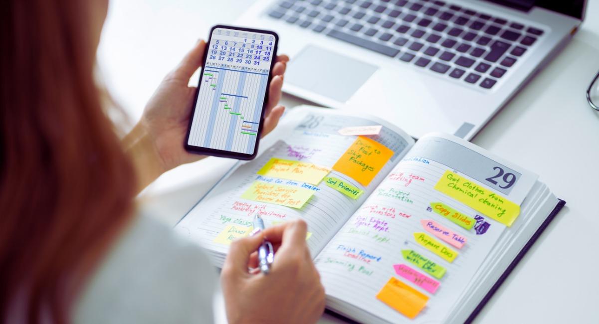 Personne consultant un calendrier sur smartphone tout en organisant un agenda papier