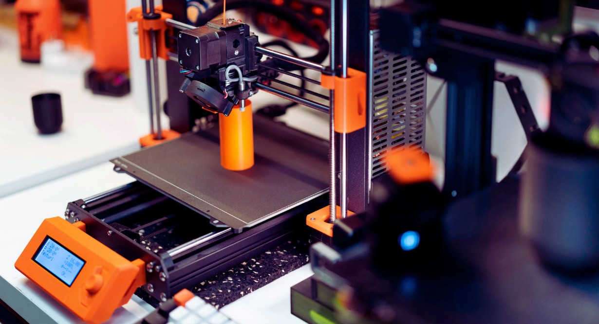 Imprimante 3D fabriquant une piece orange en plastique