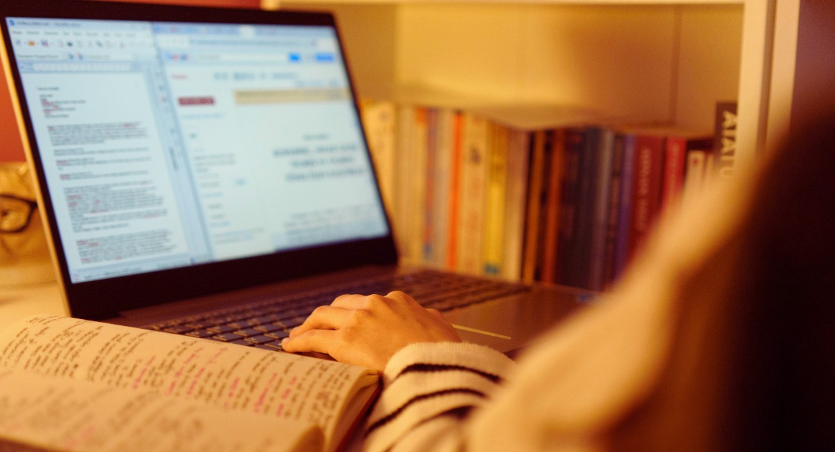 Personne consultant un article scientifique sur ordinateur portable entouree de livres