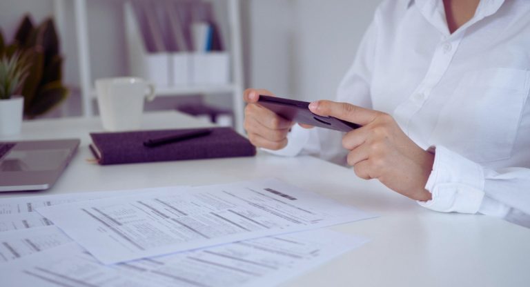 Mains photographiant un document papier avec un smartphone