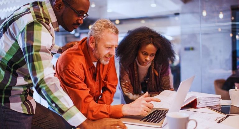 Trois collègues d'une petite entreprise étudient un document sur un ordinateur portable au bureau